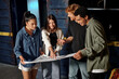 © LIGHTFIELD STUDIOS - happy woman pointing at blueprint near multicultural friends while solving mystery in escape room