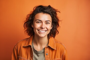 Canvas Print - Portrait of a grinning woman in her 30s sporting a rugged denim jacket against a soft orange background. AI Generation