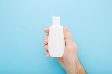 Wall Mural - Young adult man hand holding white plastic cream bottle on light blue table background. Pastel color. Care about clean and soft body skin. Daily female beauty product. Closeup. Top down view.