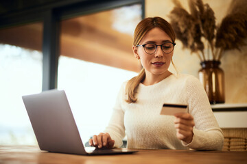 A blonde businesswoman working online, holding a credit card.