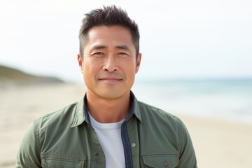 Wall Mural - Portrait of a blissful asian man in his 40s sporting a rugged denim jacket against a sandy beach background. AI Generation