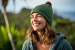 Portrait of a grinning woman in her 40s donning a warm wool beanie against a tropical island background. AI Generation