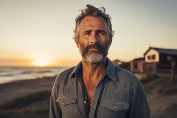 Wall Mural - Portrait of a tender man in his 50s sporting a versatile denim shirt against a stunning sunset beach background. AI Generation