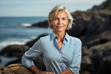 Wall Mural - Portrait of a content woman in her 60s wearing a sporty polo shirt against a rocky shoreline background. AI Generation