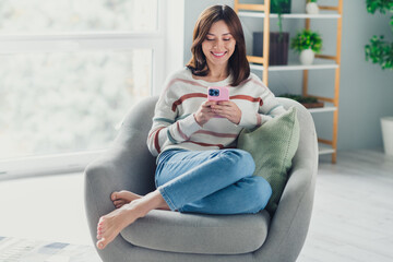 Wall Mural - full size photo of lovely cheerful girl sit chair barefoot use smart phone spacious modern flat insi