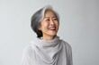 Portrait of a blissful asian woman in her 60s showing off a lightweight base layer against a minimalist or empty room background. AI Generation
