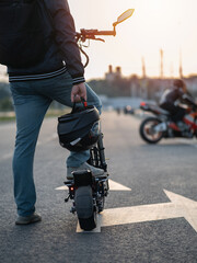 Wall Mural - Fast and powerful electric scooter on the road. The man holds the helmet in his hand. Back view