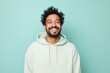 Portrait of a grinning indian man in his 20s wearing a zip-up fleece hoodie against a solid pastel color wall. AI Generation