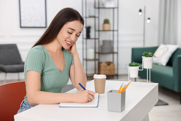 Wall Mural - Young woman writing in notebook at white table indoors