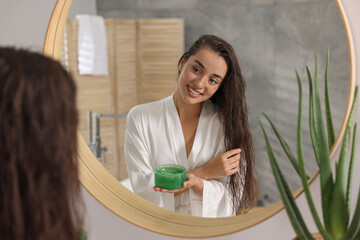 Wall Mural - Young woman applying aloe hair mask near mirror in bathroom