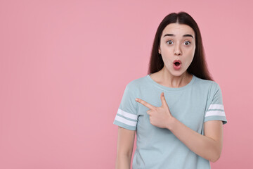 Wall Mural - Portrait of surprised woman pointing at something on pink background. Space for text