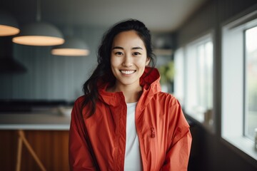 Portrait of a grinning asian woman in her 20s wearing a functional windbreaker against a crisp minimalistic living room. AI Generation