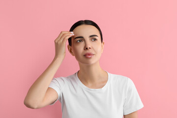 Poster - Woman with dry skin checking her face on pink background