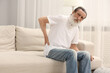 © New Africa - Senior man suffering from back pain on sofa indoors. Rheumatism symptom