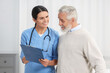 © New Africa - Smiling nurse with clipboard assisting elderly patient in hospital