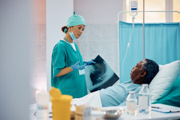 Wall Mural - Female doctor talks to black senior patient after examining his X-ray image in hospital.