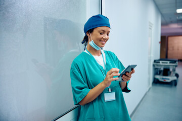 Wall Mural - Happy female surgeon text messaging on cell phone in hospital hallway.