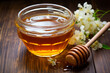 Golden acacia honey in glass bowl with honey dipper and flowers.