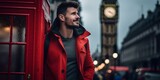 Fototapeta Big Ben - Stylish man in red jacket leaning on a classic british phone booth. iconic big ben in the background. urban portrait at dusk. AI