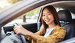 young adult woman driving a car, smiling joyfully, hands on steering wheel