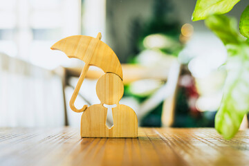 A wooden model of a businessman and an umbrella on a table is a concept for employee welfare and protection in a company.