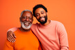 © EricMiguel - Smiling father and son in a family portrait with an orange background, showing a strong generational bond.