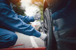 © sorapop - Skilled car mechanic in a blue work uniform, squatting next to a vehicle in an auto repair shop, fixing a tire with a focus on the hands.