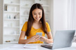 © Prostock-studio - Young Asian Woman Using Mobile Phone While Sitting At Desk With Laptop
