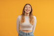 © Sergey - A young woman in a white cropped sweater on a yellow background laughing and closing her eyes.
