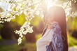 A beautiful young woman with long hair relaxes in a park with flowering trees at sunset in early spring nature.