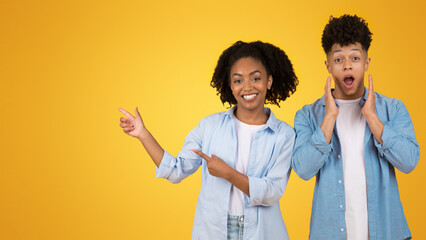 Wall Mural - Surprised young man with hands on cheeks and smiling young woman pointing to the side