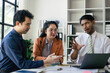 © Parichat - Two women and two men in a business meeting, Diverse business people laughing during a meeting, Business colleagues discussing strategy in the office, Business people negotiating at boardroom.