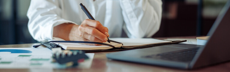 Wall Mural - Close up of business woman working on laptop, making notes in modern office interior
