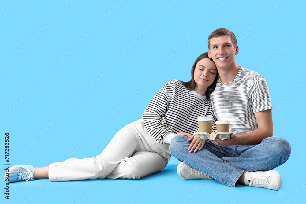 Happy young couple with coffee sitting on blue background