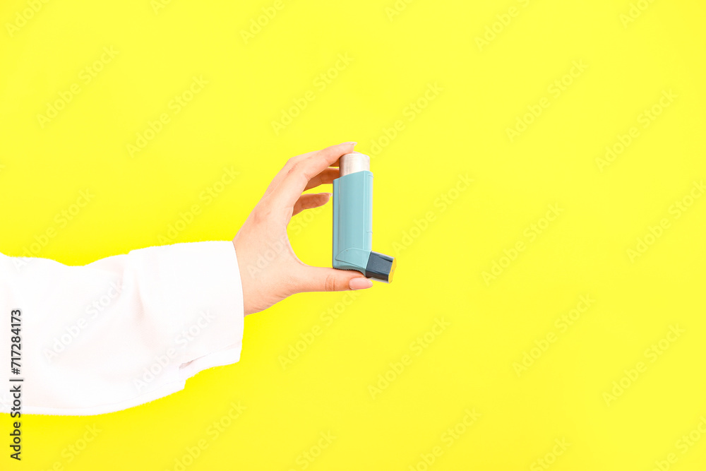 Female doctor hand with inhaler on yellow background