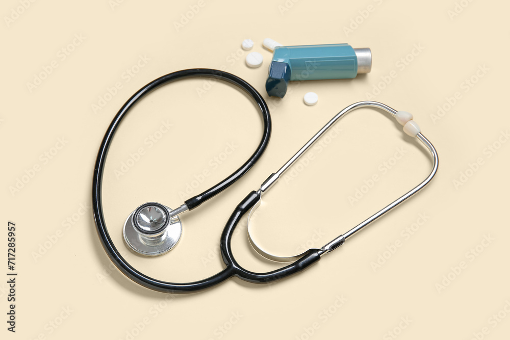 Stethoscope with asthma inhaler and pills on yellow background