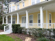 © Dolores  Harvey - The facade of a large yellow and white colored wooden middle class house with a wraparound porch on the main level. There are multiple double hung glass windows with white curtains and trim in front.