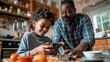 © sirisakboakaew - A funny Caucasian teen boy plays a game on his smartphone while his Black African father prepares breakfast.