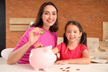 Wall Mural - Little girl with her mother putting coins into piggy bank at home