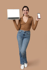 Wall Mural - Pretty young woman holding laptop and mobile phone with blank screen on beige background