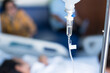 Close up set iv fluid intravenous drop saline drip in hospital room with blurry patient woman and caregiver on hospital bed.Medical treatment emergency patient.Caregiver and hopeful concept.