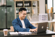 © Nuttapong punna - Young attractive man using laptop and tablet while sitting at her working place. Concentrated at work.