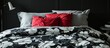 A black and white flowered coverlet on a bed with gray bedding and a red pillow.