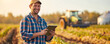 Portrait of smiling farmer in plaid shirt and cap using tablet in field