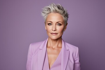 Wall Mural - Portrait of a beautiful middle aged woman with short grey hair, wearing a pink suit and looking at the camera.