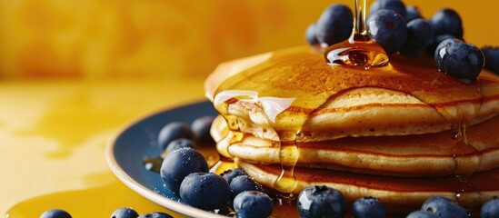 Poster - Horizontal image of maple syrup pouring onto pancakes and blueberries on yellow with copy space Food organic ingredients and healthy eating. Copy space image. Place for adding text or design