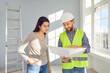 © Studio Romantic - Builder or architect in a hardhat talking to a woman. Man in a hard hat standing inside the house, talking to a young lady and showing her the construction paper plan