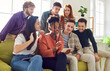 © Studio Romantic - Group of friends use mobile phone together to view photos, videos or search Internet. Multiracial young people sitting on sofa at home and looking at smartphone screen. Best pals gathering concept.