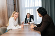 © dikushin - Joyful smiling business people having conversation sitting at desk in conference room, gathered for project discussion, looking positive, enjoy communication and teamwork together in office.