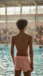 Boy standing next to an indoor public swimming pool, swimming school lesson concept with schoolboy wearing pink swim shorts